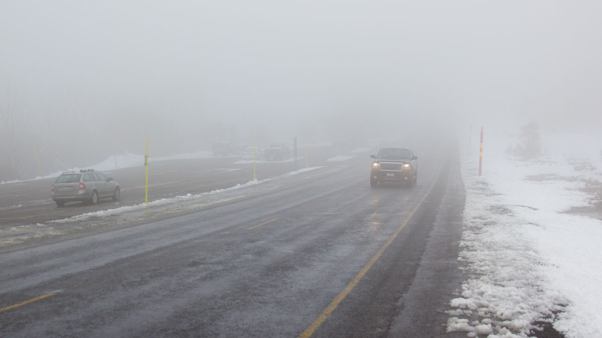 Car driving in foggy conditions with snow on side of road