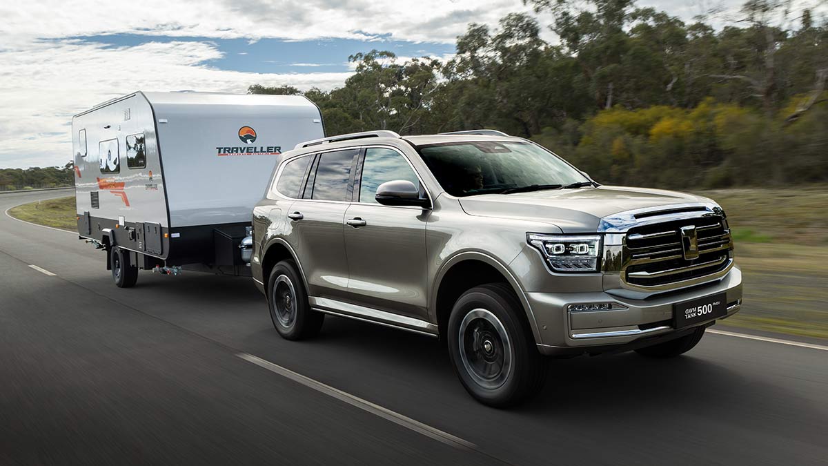 Silver GWM Tank 500 plug-in hybrid SUV with white caravan on bitumen road at Lang Lang proving ground in Victoria.