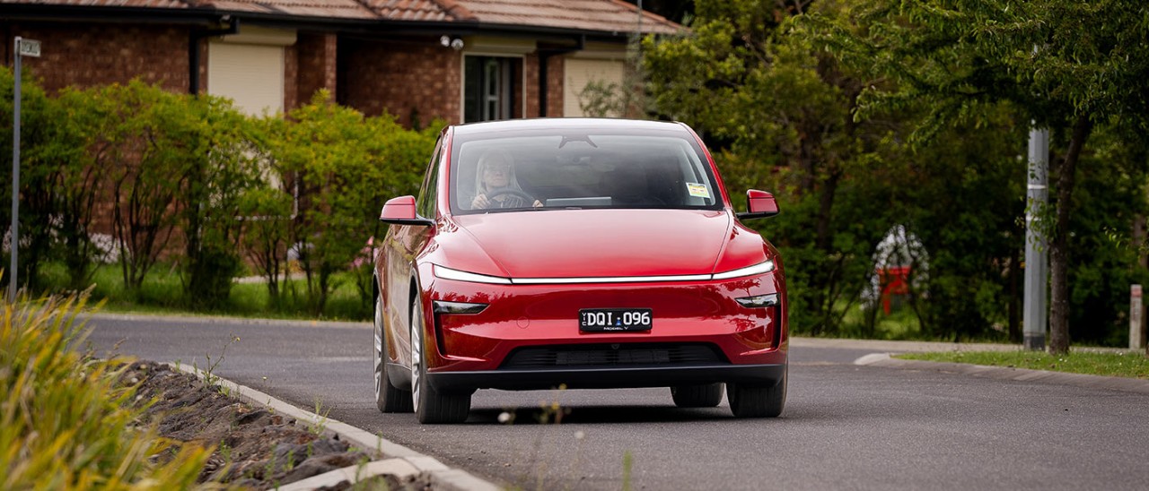 Red Tesla Model Y SUV on leafy suburban street with RACV motoring editor Andrea Matthews behind the wheel.