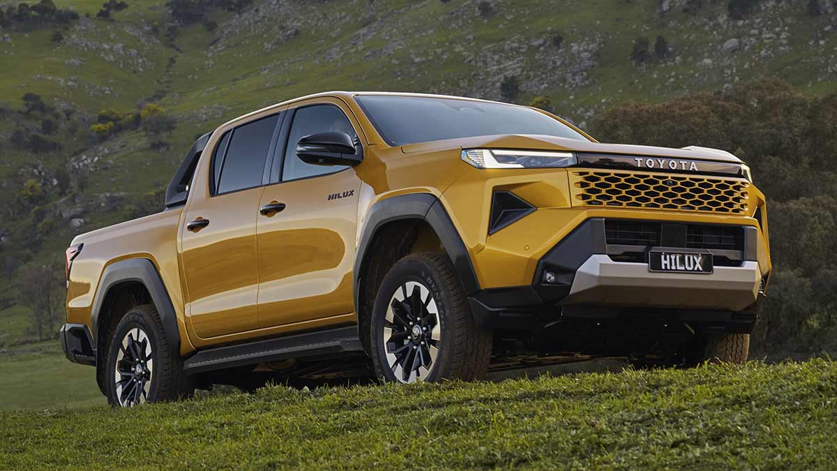 Gold Toyota HiLux SR5 dual-cab ute on off-road track next to rocky grass-covered mountain range.