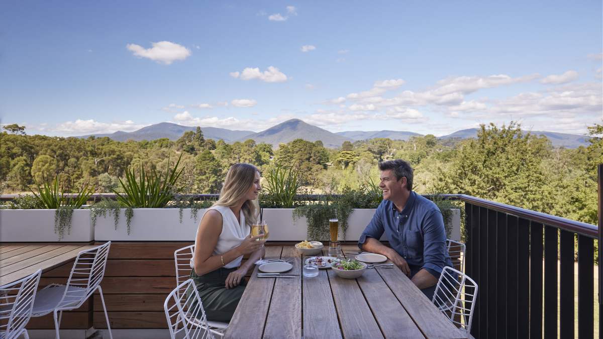 a middle-aged couple enjoy lunch and drinks on a balcony overlooking Healesville