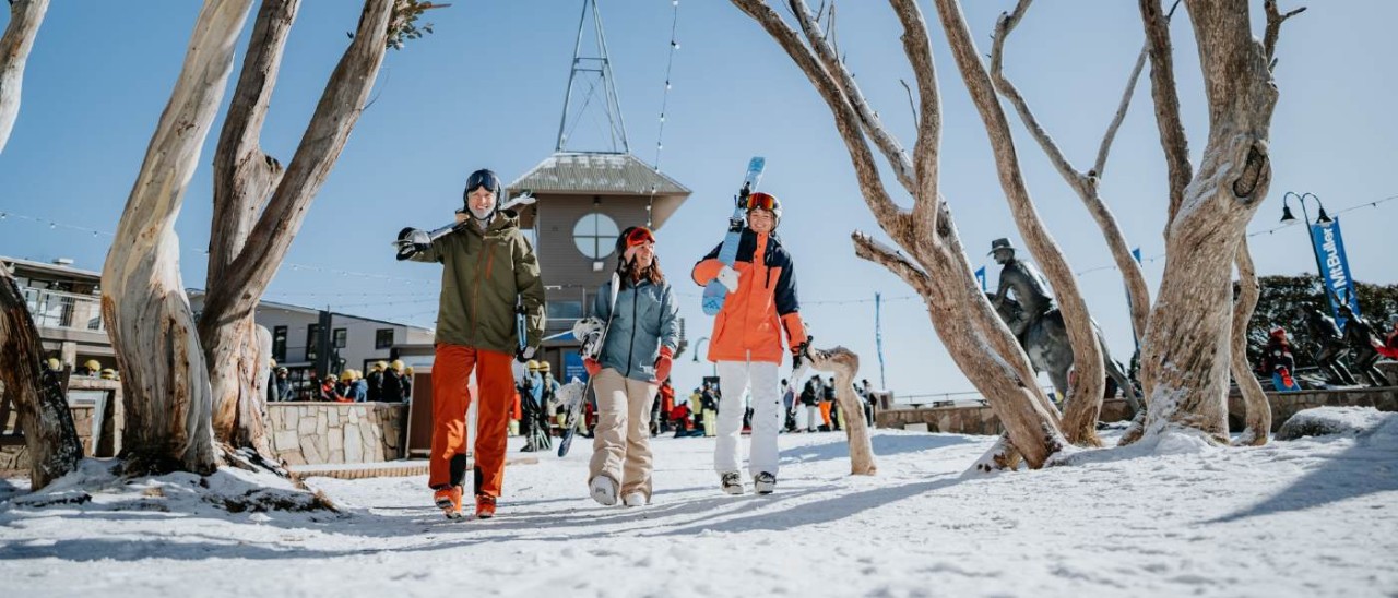 three friends dressed in snow gear carrying skis at Mt Buller, Victoria