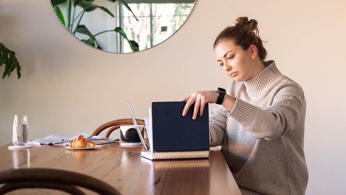 Woman at kitchen table looking at diary and computer