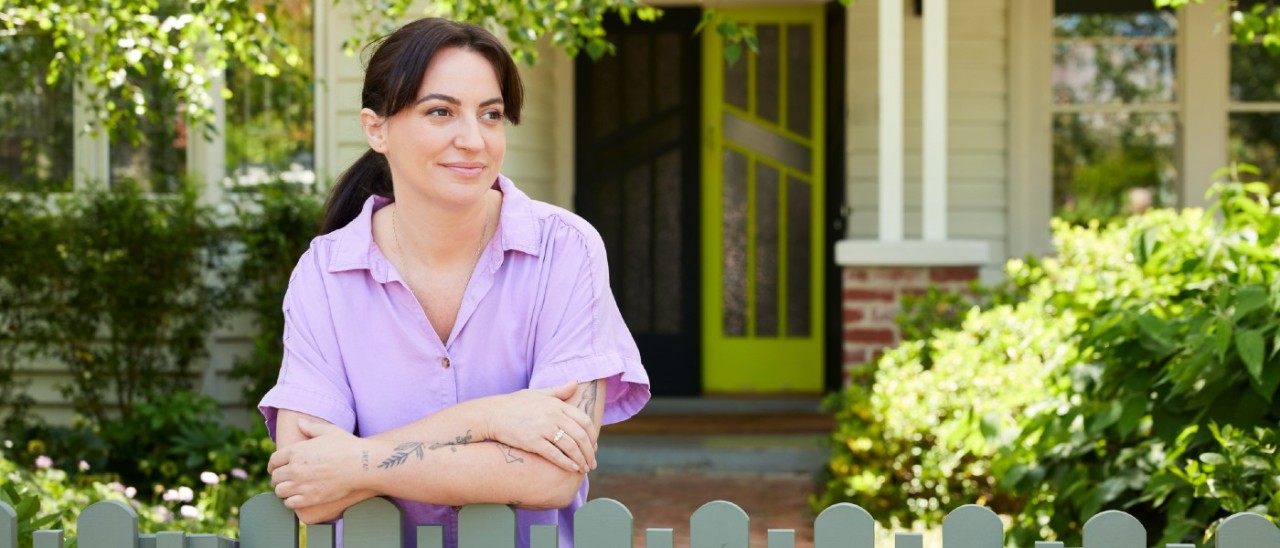 young woman leaning on fence in front of her house