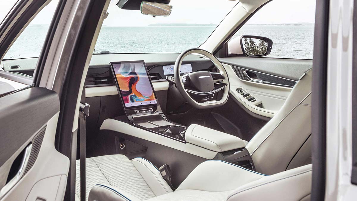 Jaecoo J5 EV front cabin as seen from rear left door, showing two-tone cream/grey trim and large portrait centre touchscreen.