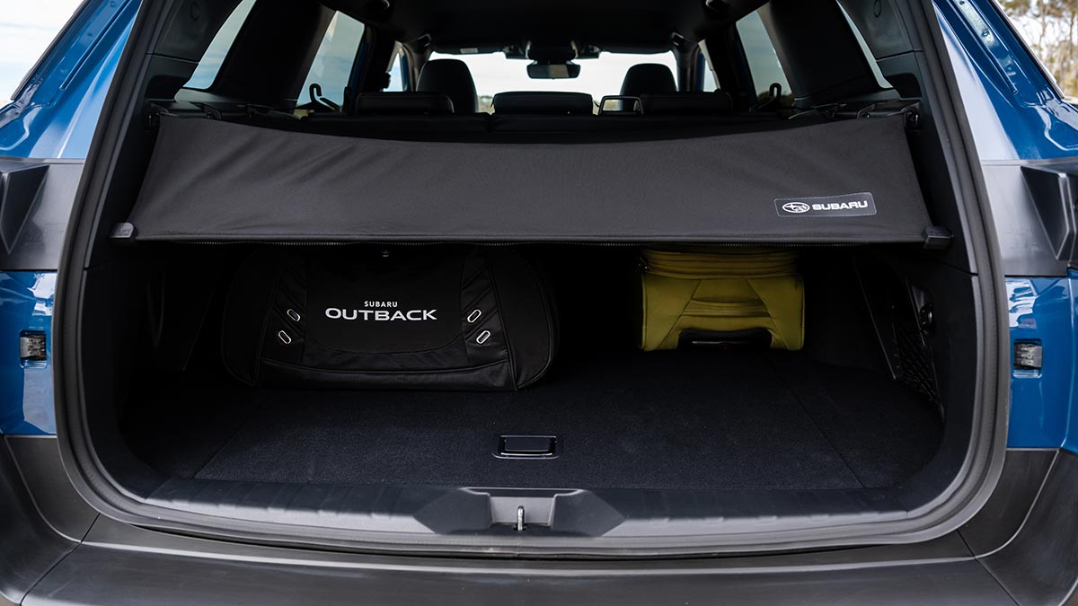 Tailgate open in blue Subaru Outback Wilderness SUV with black and yellow bags and new soft cargo cover.