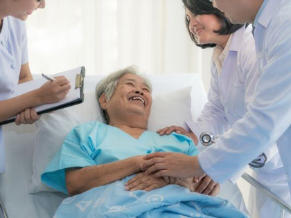 Three doctors speaking with an ederly woman in a hospital bed. 
