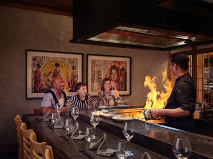 Family enjoying dinner at RACV Royal Pines Arakawa's teppanyaki table while watching chef flambé hot plate.