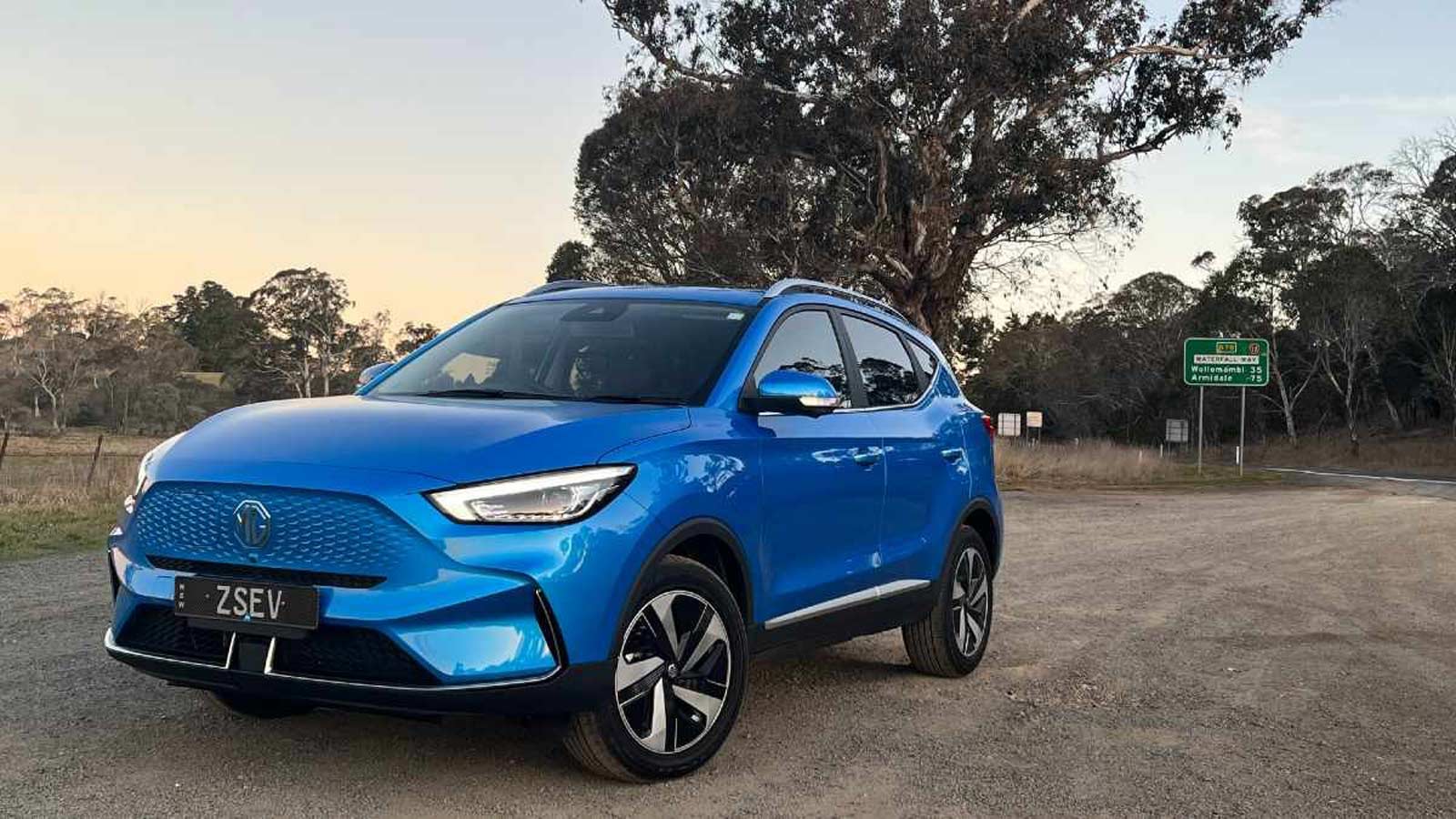 A blue MG parked on a dirt road off the highway.