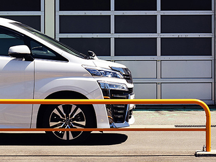 A white car parked near an orange metal fence.
