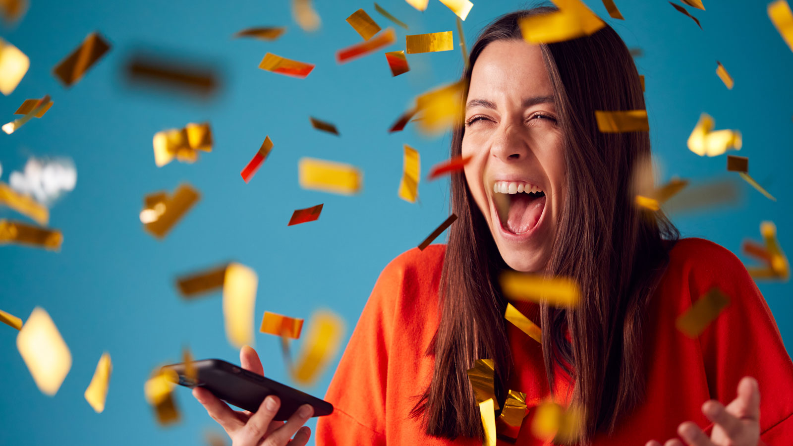 Woman with mobile phone winning a prize and showered with gold confetti
