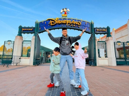 Father and two kids posing happily outside Disneyland Paris.