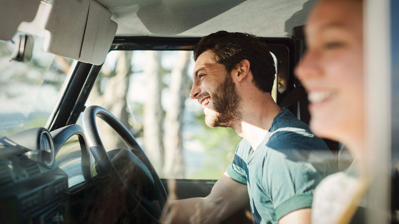 Young couple smiling in the front seats of a vehicle.