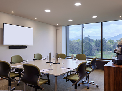 Conference room with square 8-seat table, projector screen and large windows featuring nature views.
