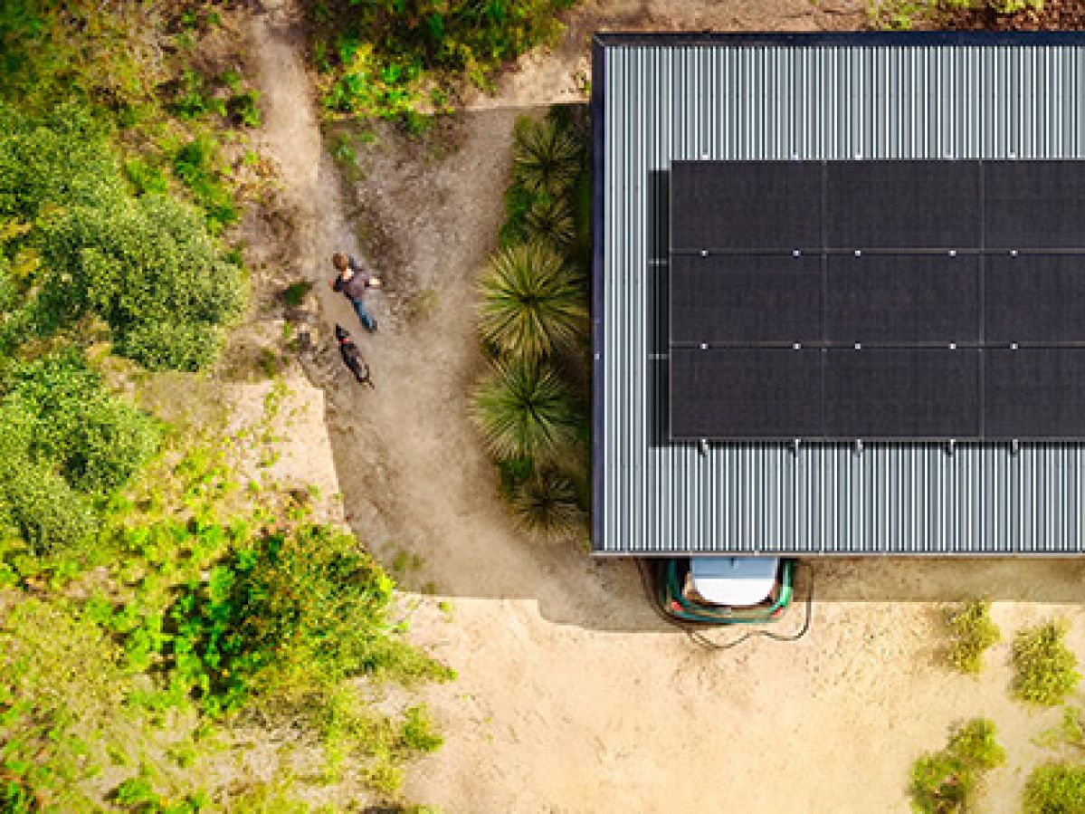 A person and their dog walking on a dirt path beside a building with RACV-installed solar panels on its roof.