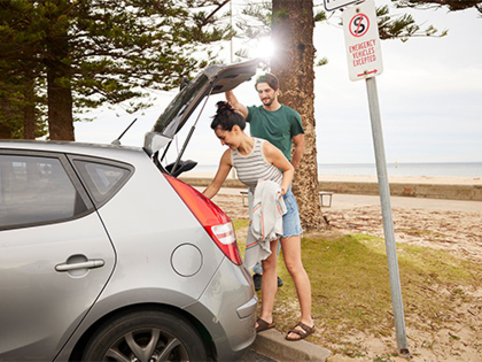 Couple taking a towel out of their boot, while at the beach.