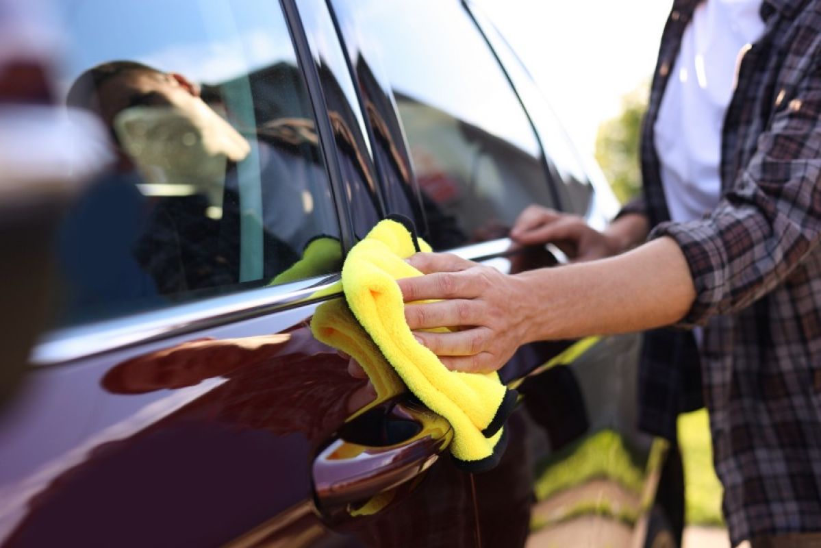 A person cleaning a car and polishing its paint using a bright yellow chamois