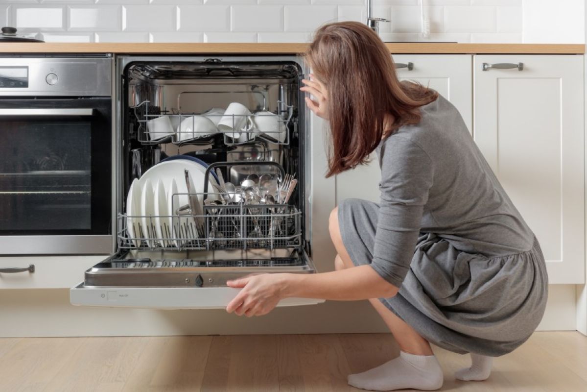 woman crouching in kitchen looking into open dishwasher