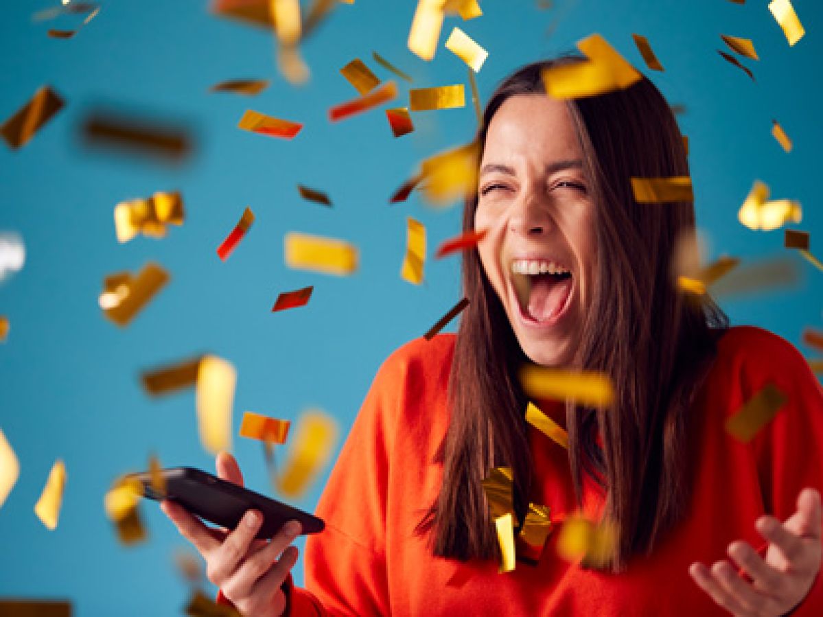 woman with mobile phone winning a prize and showered with gold confetti