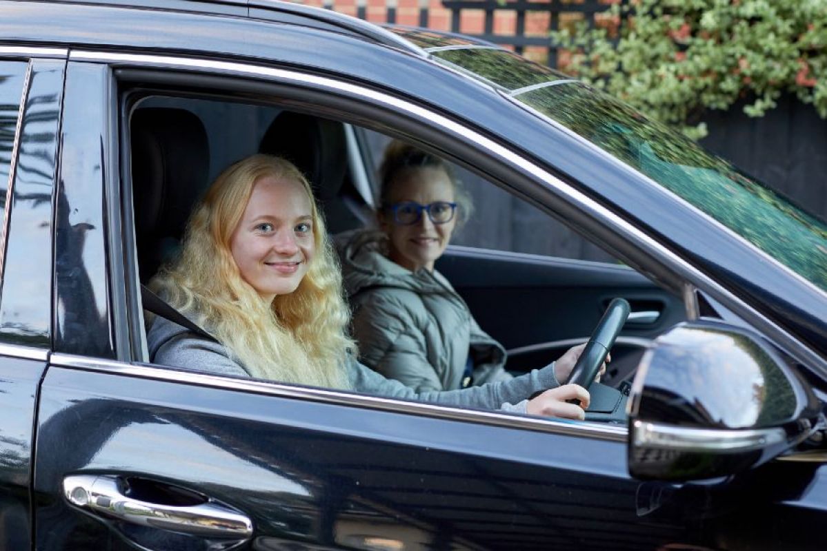 learner driver holding car wheel with her supervisor in passenger seat