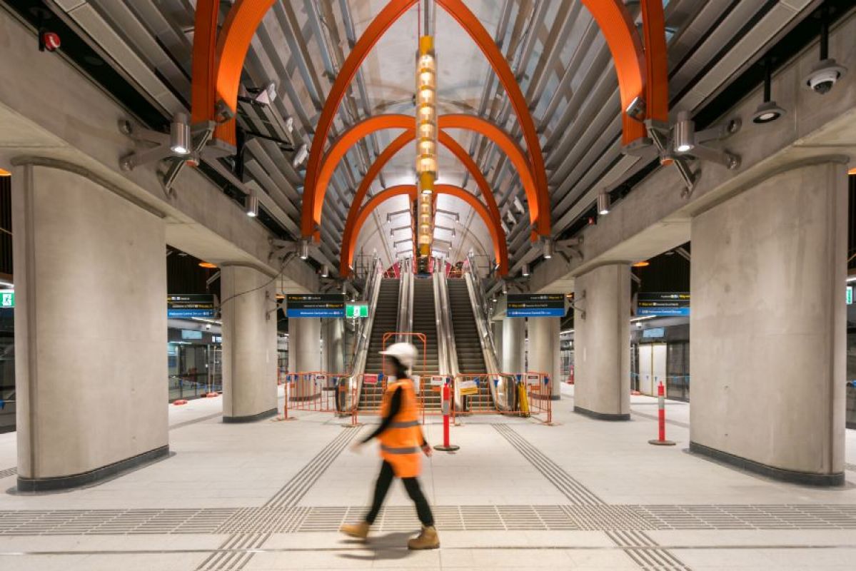 A construction worker wearing an orange high vis vest walking on a platform at State Library Station