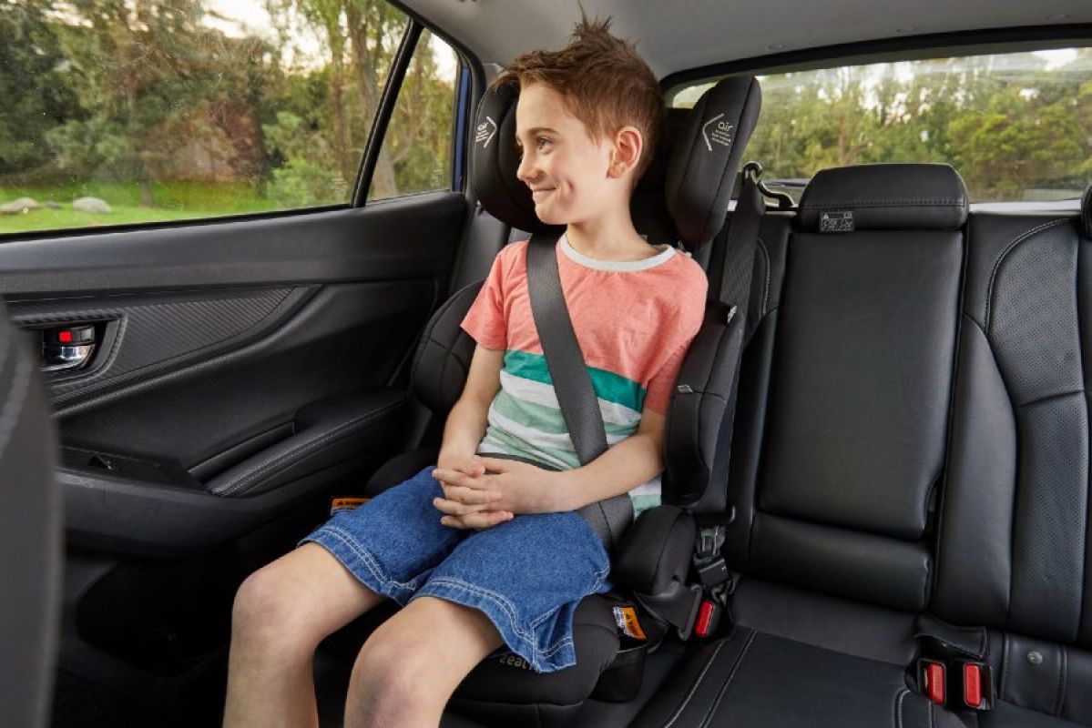 A young school-aged boy sits smiling in a booster seat secured in a car's back seats