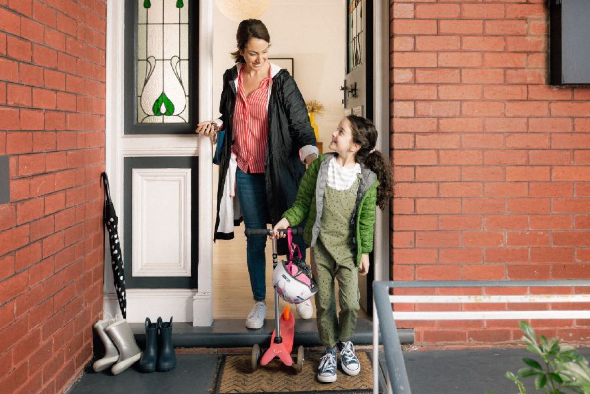 mother and daughter exiting their brick home in winter coats