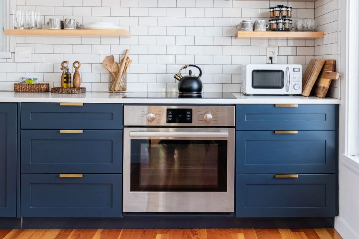 A modern kitchen featuring dark blue cabinetry, white subway tiles and a modern oven with induction cooktop
