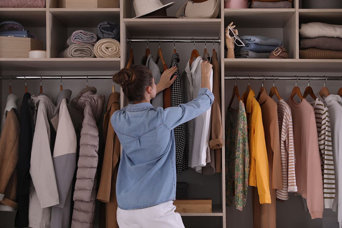Young woman with brown hair and blue shirt choosing white shirt on hanger from wardrobe