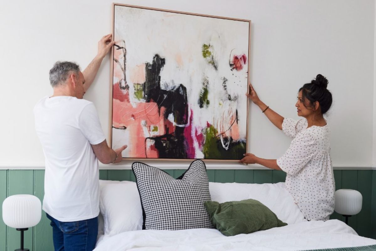 man and woman hanging a painting over a bed