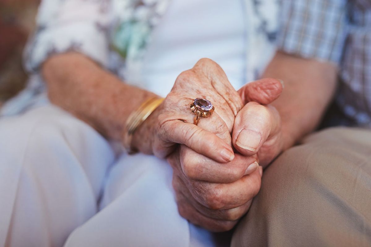 elderly couple holding hands showing engagement ring 