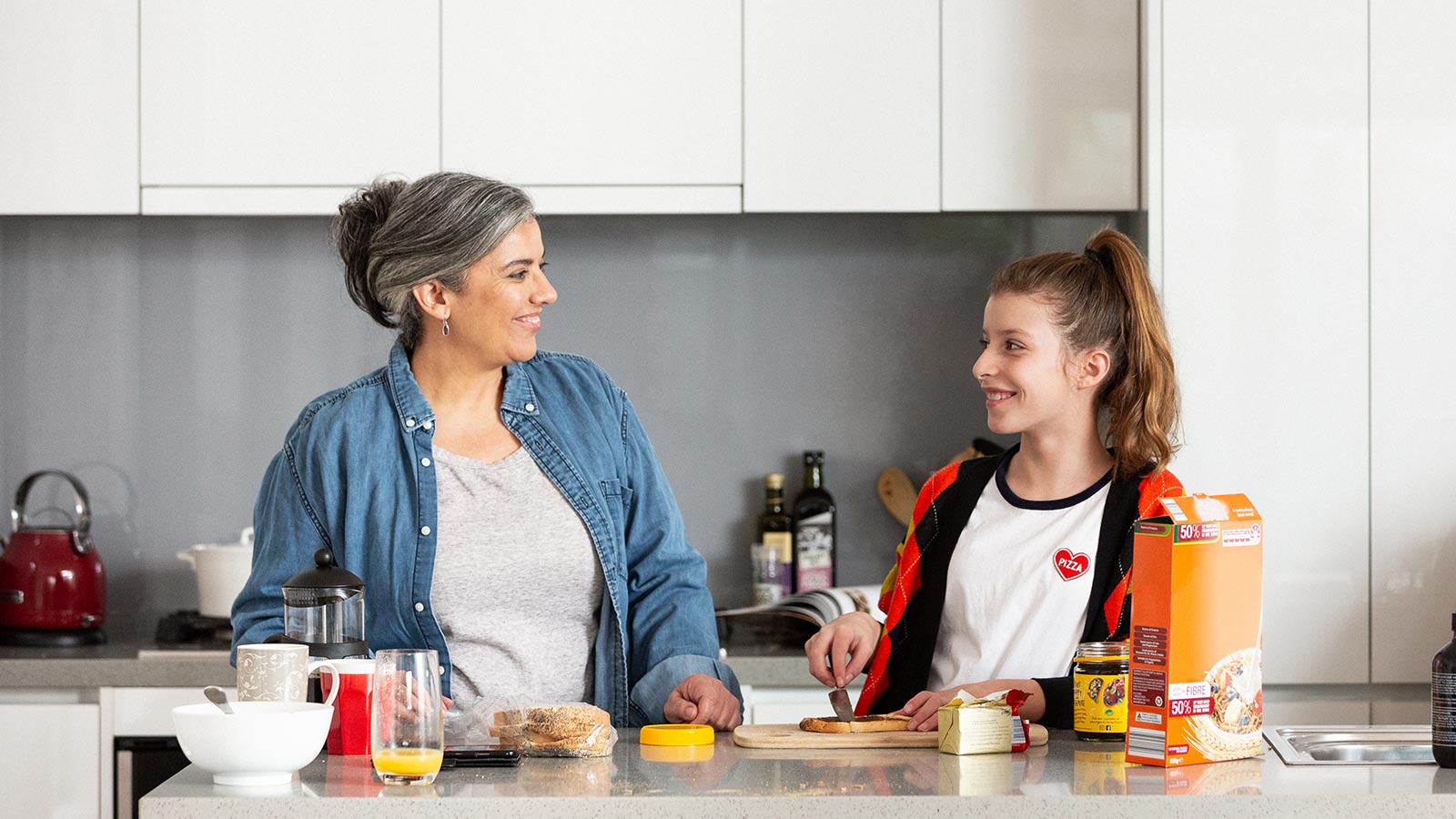 Mother and daughter standing at kitchen bench making sandwiches.