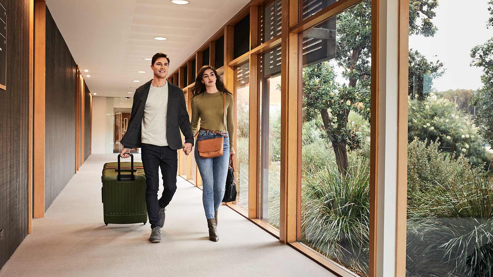 Couple wheeling their luggage and holding hands while walking down a hallway at RACV Inverloch Resort.