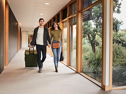 Couple wheeling their luggage and holding hands while walking down a hallway at RACV Inverloch Resort.