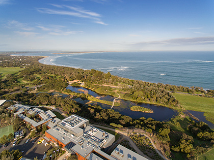RACV Inverloch Resort on a sunny day, in front of green trees and fields, and the beach.