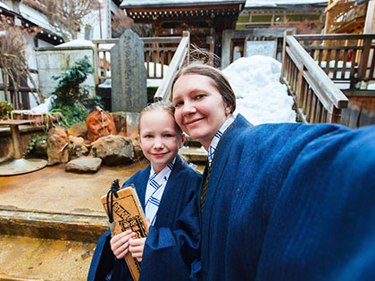 Mother and daughter wearing yukatas and taking selfie at a street of onsen resort town in Japan.