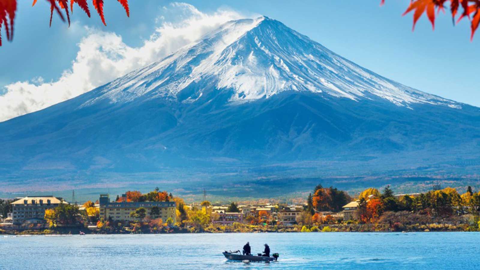 Snow capped Mount Fuji behind a small town and lake.