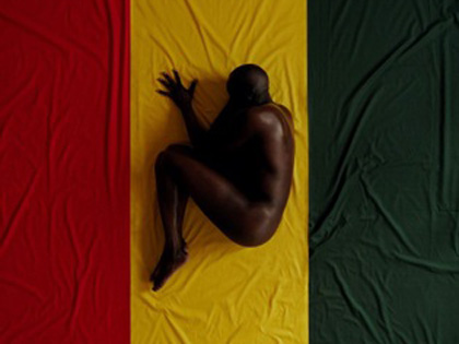 A man laying naked on the flag of Kenya.