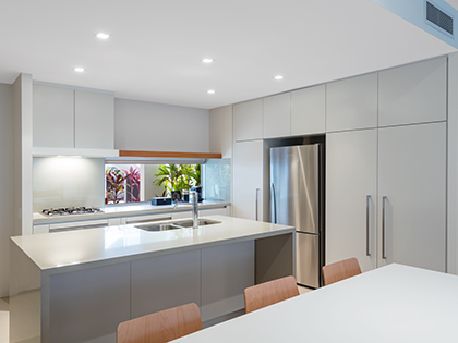 Kitchen and dining area in RACV Noosa Resort's 3-bedroom Sanctuary Apartment, featuring a dining table, kitchen island, cooktop and fridge.