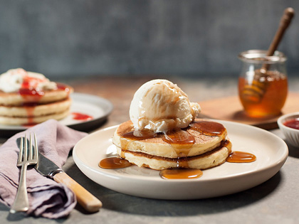 Multiple stacks of pancakes on a table with a napkin, knife and fork. 