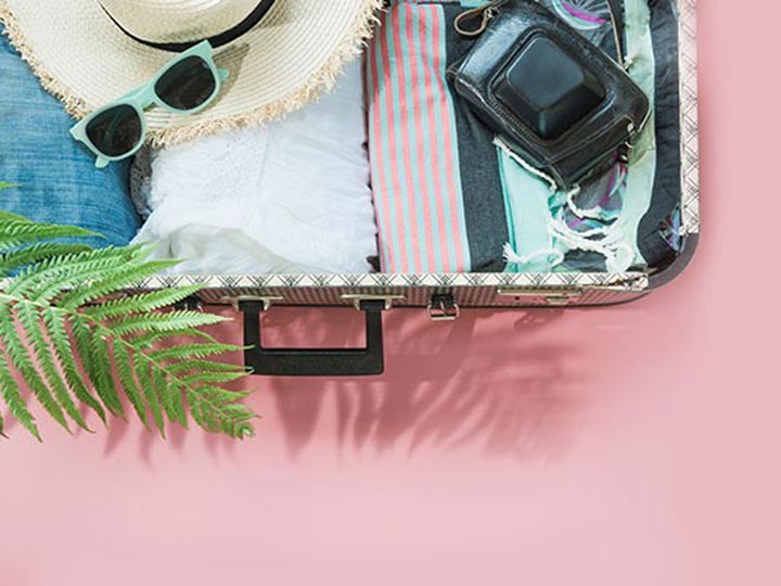 Pink background with a suitcase filled summer items.