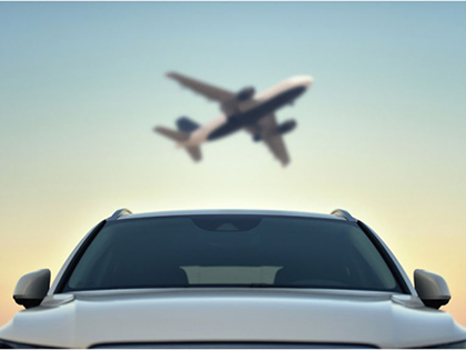 A silver car, with a plane taking off in the distance.