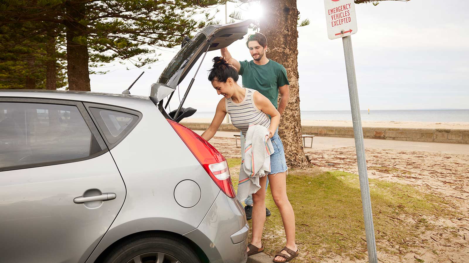 Two people taking a towel out of their car boot, while at the beach.
