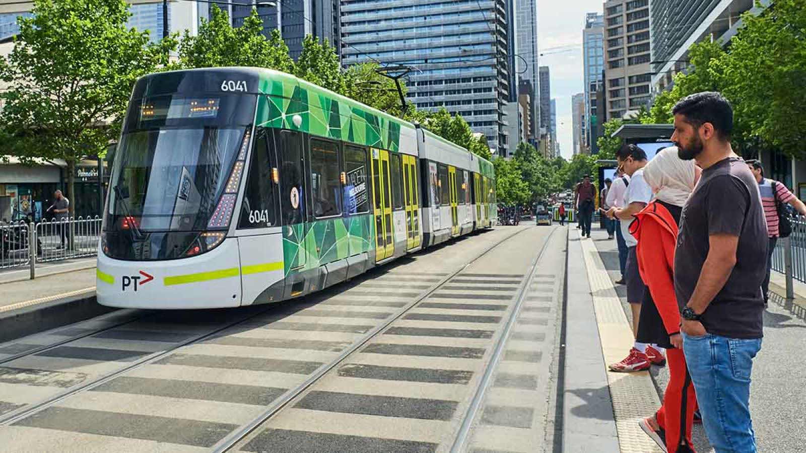 Group of people standing at a tram stop as a tram approaches.