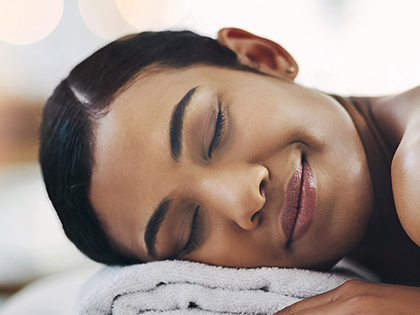 Woman lying down on a massage bed at RACV One Spa, smiling with her eyes closed.