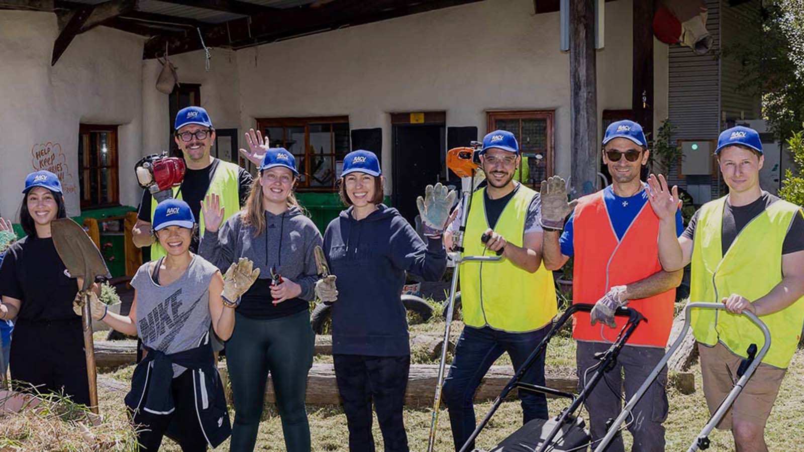 RACV team members at a garden volunteering day, wearing blue caps and holding shovels.