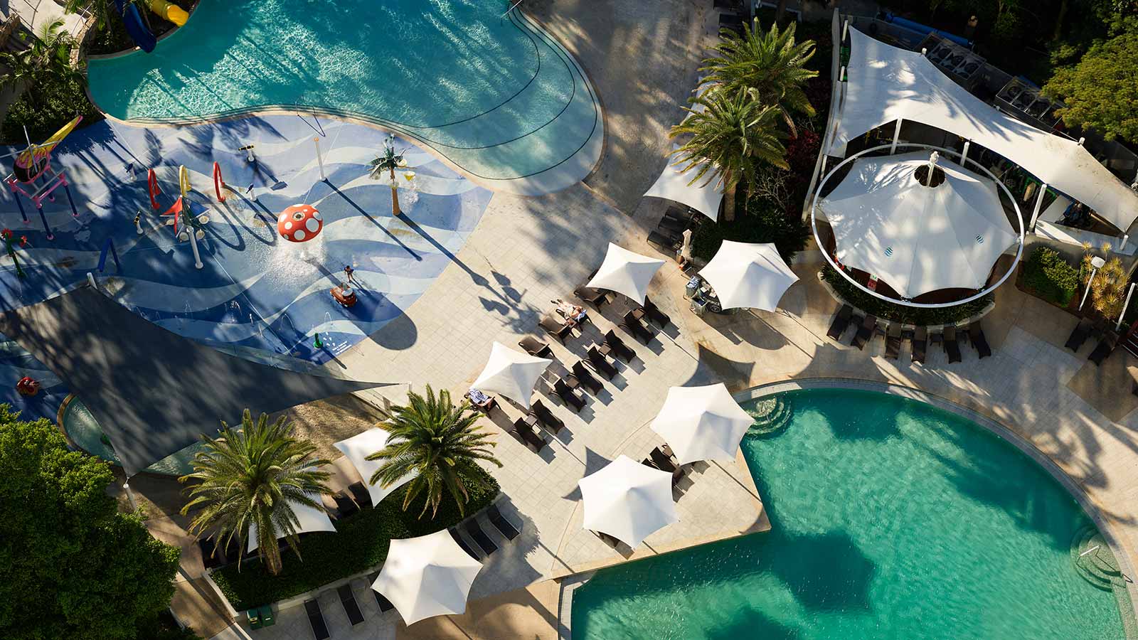 Royal Pines outdoor pool area, including lagoon pool, water park and green palm trees.