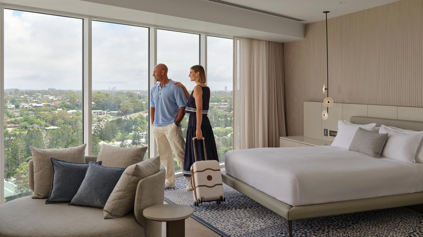 Couple standing in the Royal Pines suite, smiling while looking at the view outside the window.