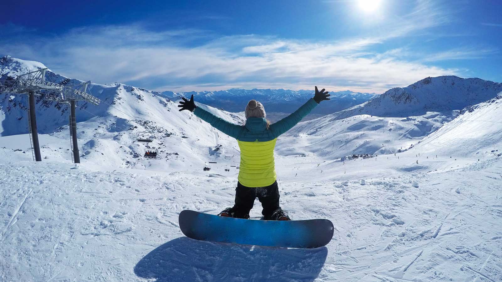 Woman with a snowboard on a mountain in the snow with her arms spread open to the view. 