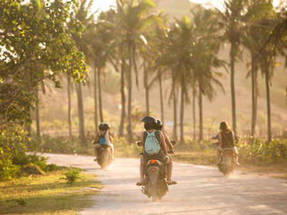 People riding three motorcycles on a road lined wiith palm trees in Bali.